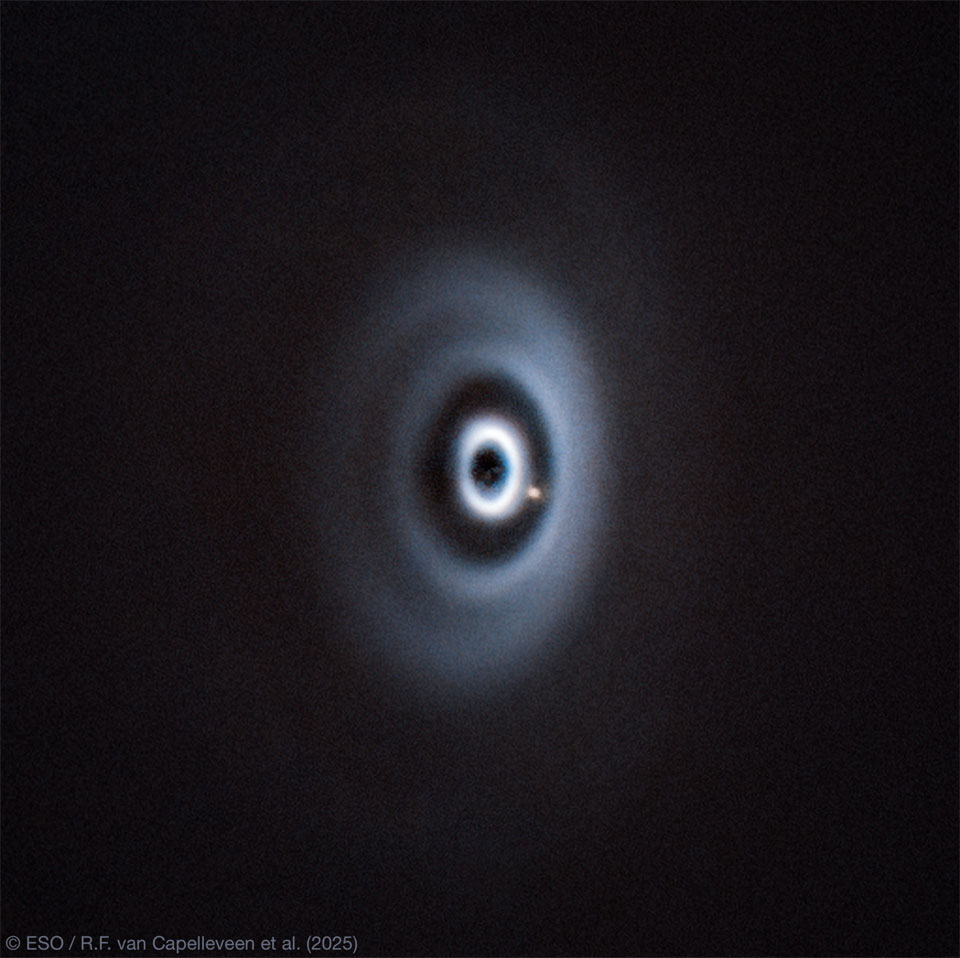 A dark field has a series of light-colored elliptical rings in the center. Between two of the rings is a yellow-colored spot. Please see the explanation for more detailed information.