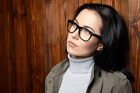 75752560-young-woman-in-glasses-standing-by-the-wooden-wall-business-casual-style-optics-.jpg